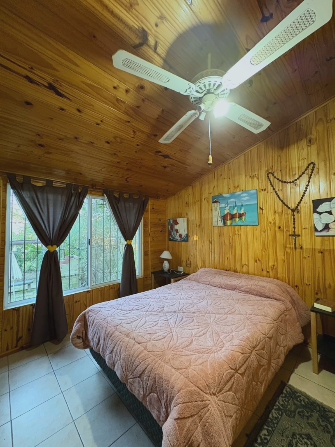 Dormitorio principal con cama matrimonial, paredes de madera y ventanas al exterior.