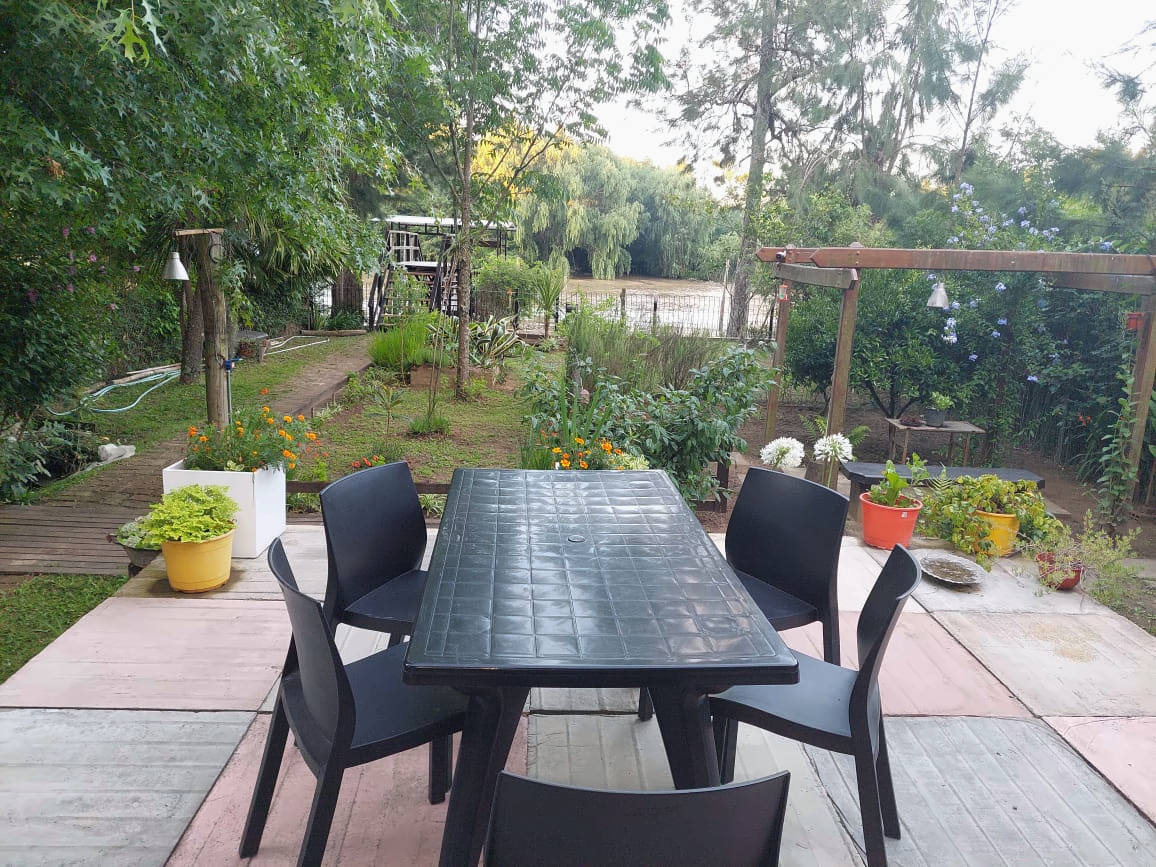 Mesa con sillas en el parque, rodeada de vegetación y con el río al fondo.