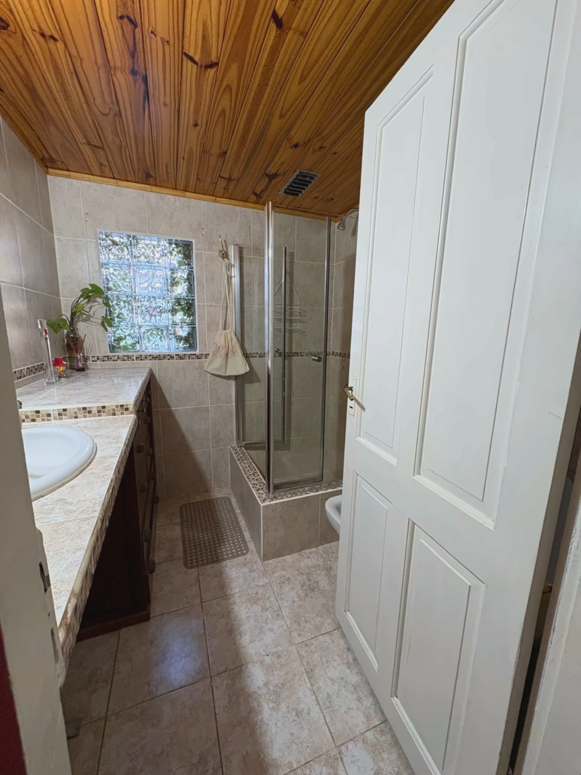 Primer baño interior con mesada, ventana y ducha con mampara.